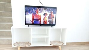 Een moderne woonkamer met een witte tv-meubel, een flatscreen televisie en een bijzondere witte tafel met houten poten.