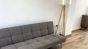Een grijze bank met houten poten en een witte tafel met houten poten in een kamer met houten vloer.