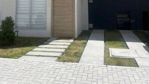 Een modern, tweelaags gebouw met een garage, een houten deur en een kleine tuin met een pad.