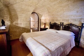 Une chambre avec un mur en pierre, un lit en bois avec une tête de lit, une table de chevet et un miroir.