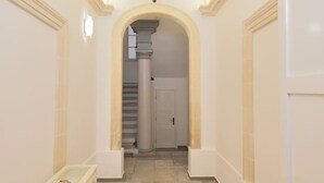 A hallway with a marble floor, white walls, and a central column leading to a staircase. - The George Studio at Grand Harbour View Flats (Il-Furjana)