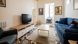 Un soggiorno con televisione, un divano blu, un tavolino da caffè e un pavimento decorato.
