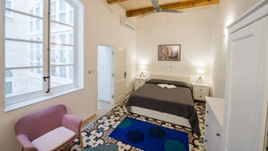 Una camera da letto con un letto, una sedia, una finestra, una ventola a soffitto e una porta.