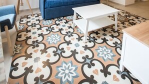 Un soggiorno con un divano blu, un tavolino da caffè bianco, piastrelle a pavimento decorate e due quadri appesi al muro.