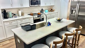 Moderni keittiö, jossa on valkoiset kaapit, ruostumattomasta teräksestä valmistettu jääkaappi, mikroaaltouuni ja pesuallas.