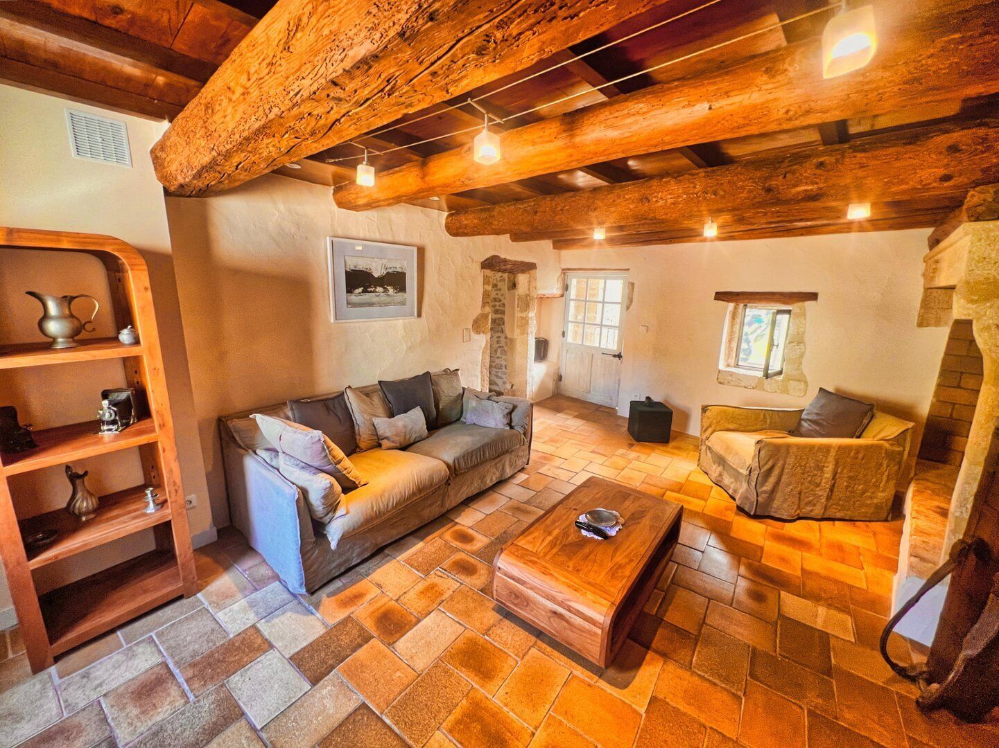 Ein gemütliches Wohnzimmer mit Holzbalkendecke, einer Couch, einem Couchtisch und einem Kamin aus Stein.