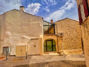 A building with a stone facade, a glass entrance, and a small air conditioning unit mounted on the wall. - P’tit Coin Paradis – Heated Pool & Hot Tub (Saint-Hippolyte-de-Montaigu)