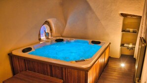A hot tub with a wooden bench, a small shelf with towels, and a radiator in a corner.