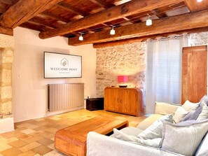 Uma sala de estar acolhedora com teto de madeira, parede de pedra, um sofá, uma mesa de centro e um letreiro com a mensagem 'WELCOME HOST'.