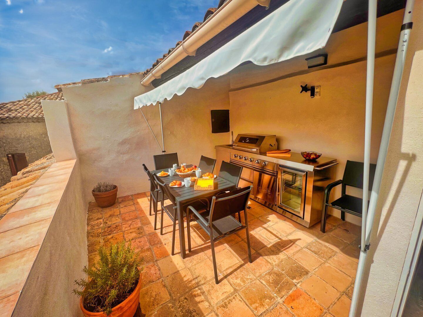 Eine Terrasse im Freien mit Esstisch, Grill und Topfpflanzen.