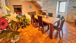 A dining area with a wooden table and chairs, a hexagonal tiled floor, a stone wall, and a staircase leading to an upper level.