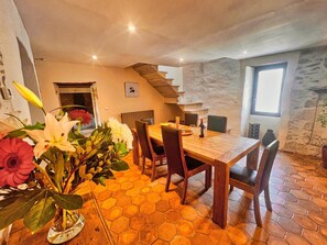 A dining area with a wooden table and chairs, a hexagonal tiled floor, a stone wall, and a staircase leading to an upper level. - P’tit Coin Paradis – Heated Pool & Hot Tub (Saint-Hippolyte-de-Montaigu)