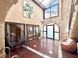 An indoor patio with a wooden deck, seating, and a large abstract painting. - P’tit Coin Paradis – Heated Pool & Hot Tub (Saint-Hippolyte-de-Montaigu)
