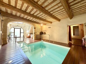 An indoor swimming pool with wooden beams, stone walls, and a view of the outside. - P’tit Coin Paradis – Heated Pool & Hot Tub (Saint-Hippolyte-de-Montaigu)