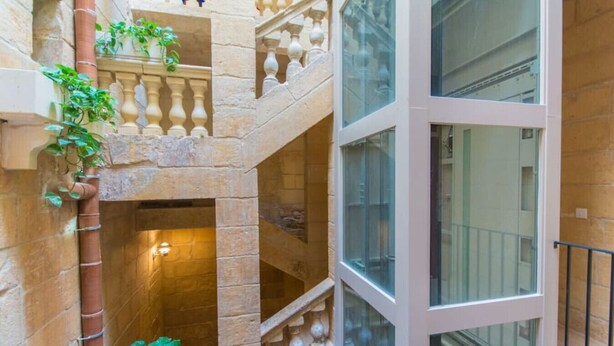 A multi-level interior with stone walls, a central staircase, and large windows. - Casa San Carlo Valletta - Azure (Valletta)