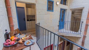 A balcony with a table set for a meal, a kitchen area, and a small balcony with a railing. - Casa San Carlo Valletta - Azure (Valletta)