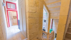 A stone corridor with a wooden floor, leading to a room with a red door and a balcony with a stone railing. - Casa San Carlo Valletta - Azure (Valletta)