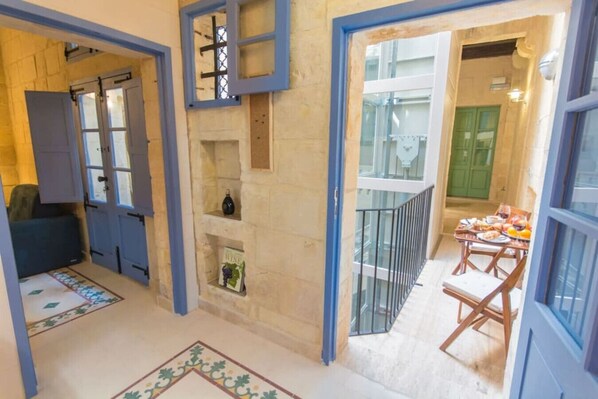 Une pièce avec un mur en pierre, une bibliothèque, une petite table avec une chaise et un balcon doté d’une balustrade.