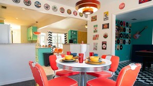 Un comedor de estilo retro con una mesa redonda, sillas rojas y una colección de discos de vinilo en las paredes.