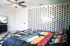 A bedroom with a bed, a ceiling fan, a wall of circular stickers, and a television on a dresser. - The Jukebox Joint | Pool table | Ping-Pong | 3 TVs (Del Rio)