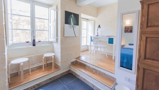A room with a large window, a desk with a chair, a small stool, and a wooden cabinet.