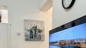 Moderni olohuone, jossa on seinäkaapissa litteänäyttöinen televisio, seinällä maljakkoaiheinen taulu ja television yläpuolella oleva kello.