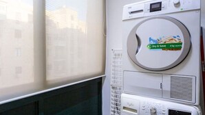 Un lavadero pequeño con lavadora y secadora de carga frontal, una ventana con persianas y un radiador.