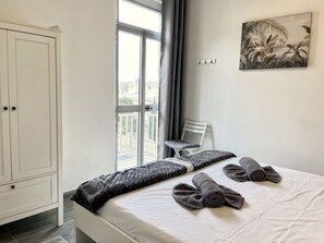 A bedroom with a bed, a chair, a wardrobe, and a window with a view. - Matthias Two Bedroom - Steps away from Valletta (Il-Furjana)