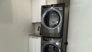 A compact laundry room with two stacked front-loading washing machines, a white sink, and a laundry basket.