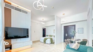 Ein modernes Wohnzimmer mit einem großen Flachbildfernseher, einem türkisfarbenen Sofa und einem Essbereich mit Tisch für zwei Personen.