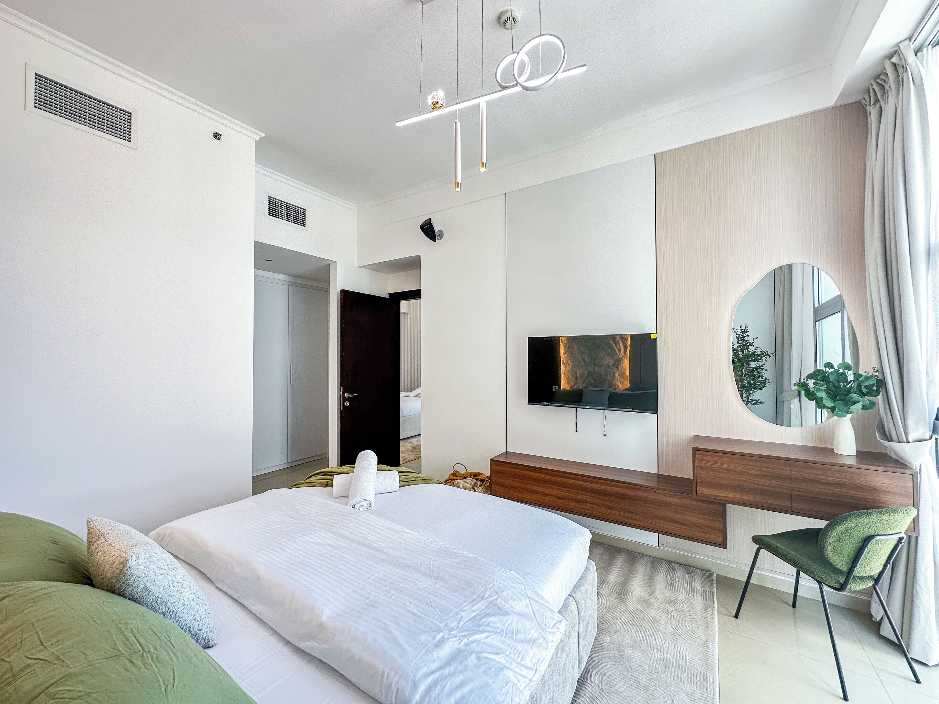 Un dormitorio moderno con una cama grande, un televisor montado en la pared, un espejo y una planta sobre una mesita de noche.
