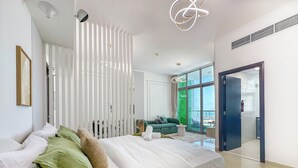 Ein modernes Schlafzimmer mit einem großen Bett, einem grünen Sofa und Blick ins Freie durch große Fenster.