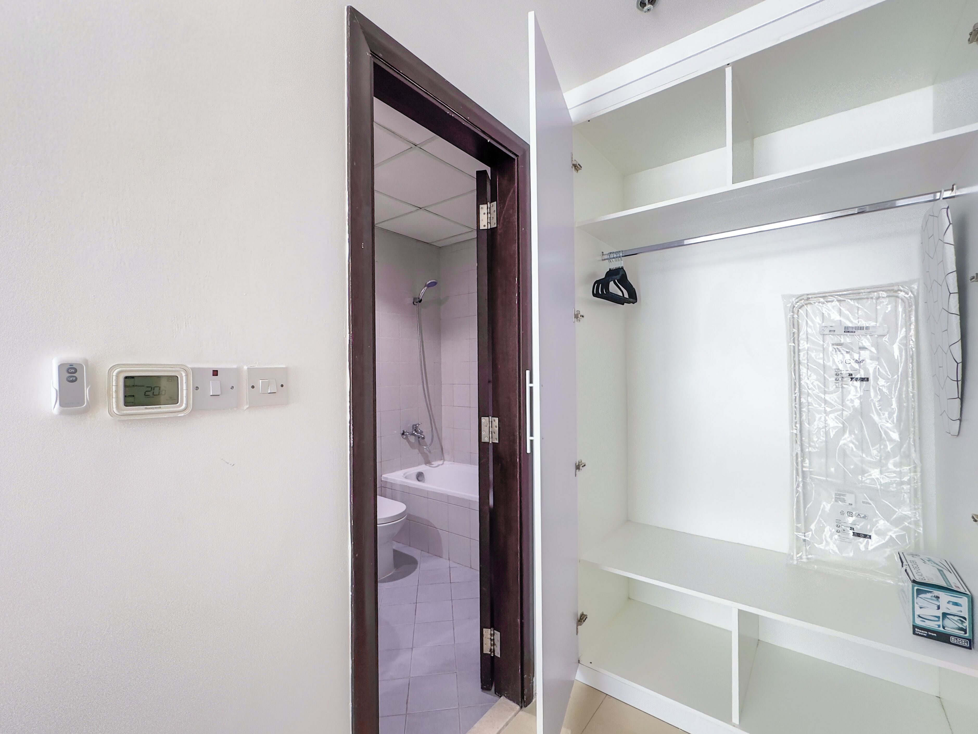 A bathroom with a shower, toilet, and a shelf with a shower caddy and a plastic-wrapped item.