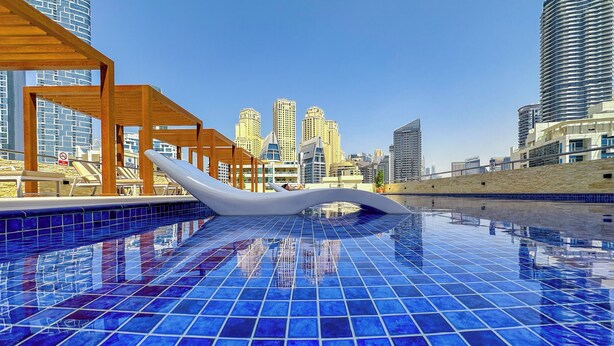Ein Swimmingpool mit blauen Fliesen, umgeben von modernen Gebäuden und einer Holzhütte.