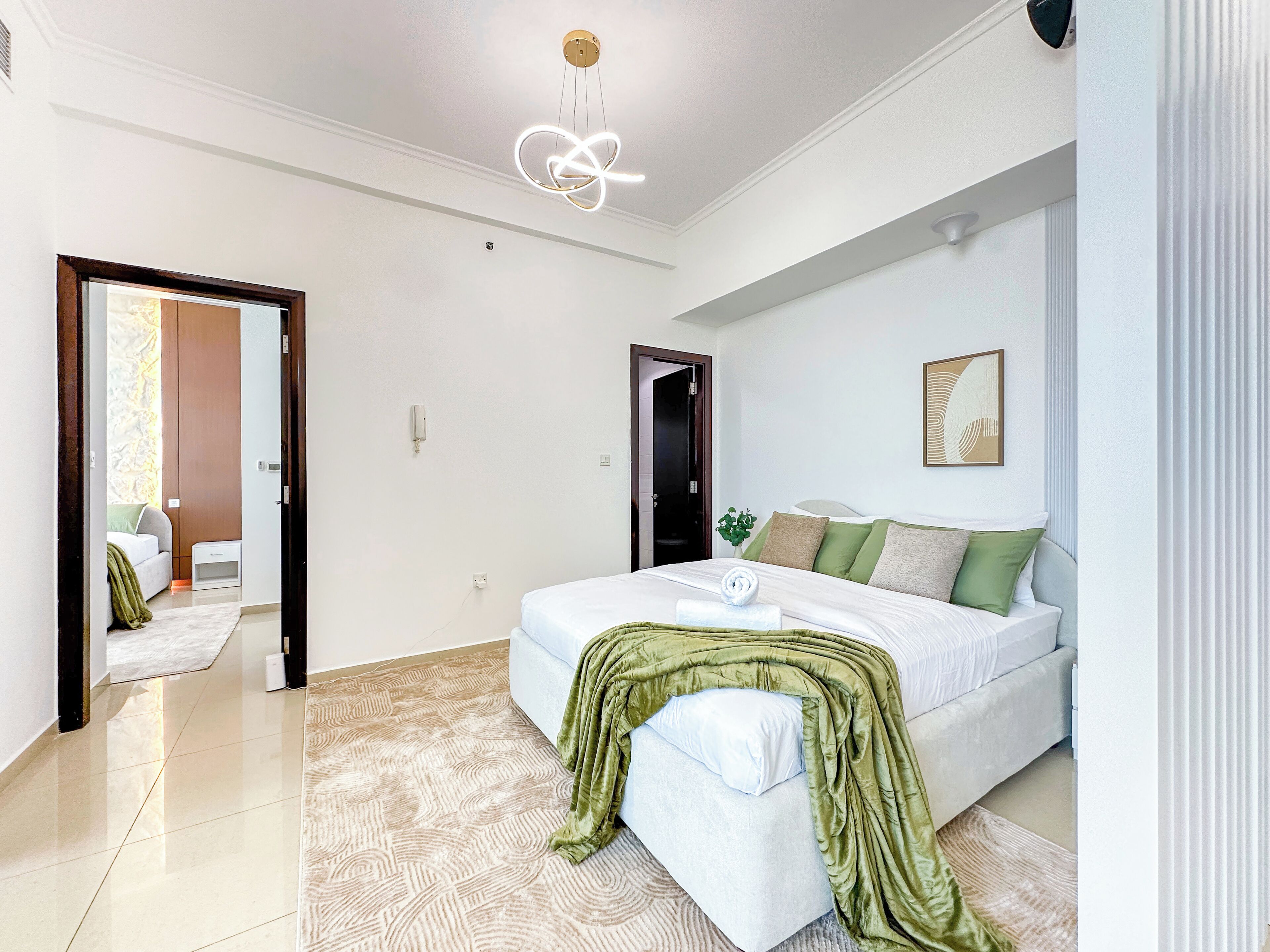 A modern bedroom with a large bed, a green throw blanket, and a ceiling light fixture.