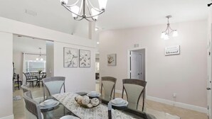 A dining area with a glass table, chairs, and a chandelier. - Heated Pool/ 4 Bedrooms (Naples)