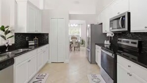 A modern kitchen with white cabinets, a black countertop, and a microwave. - Heated Pool/ 4 Bedrooms (Naples)