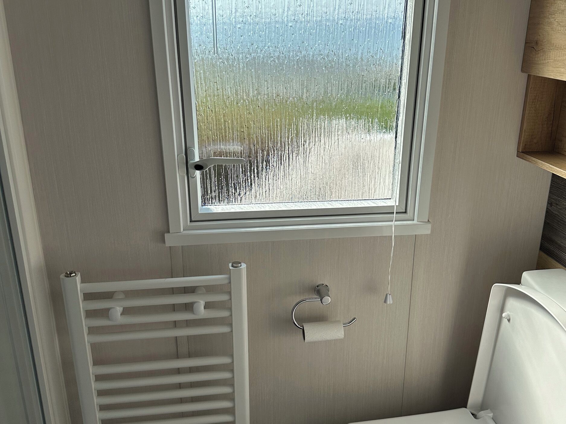 Een badkamer met een raam, een handdoekrek en een toiletrolhouder.