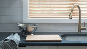 A kitchen with a modern sink, a colander, and a cutting board on the counter.