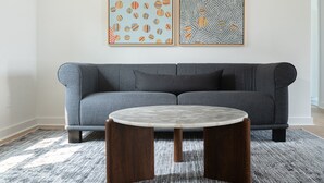 A modern living room with a grey sofa, a round marble coffee table, and two abstract paintings on the wall.
