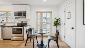 A modern kitchen with stainless steel appliances, a dining table with chairs, and a potted plant.