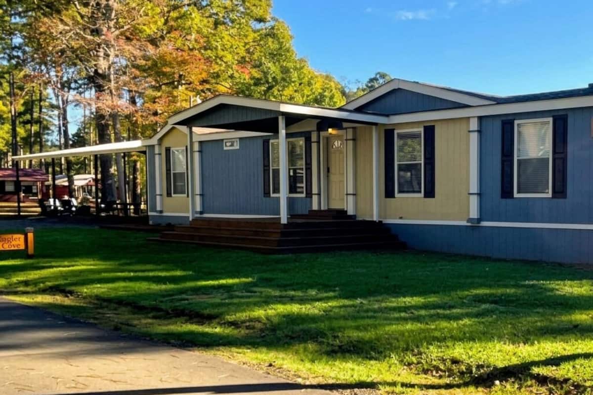 A single-story mobile home with a front porch, a small front yard, and a clear sky.