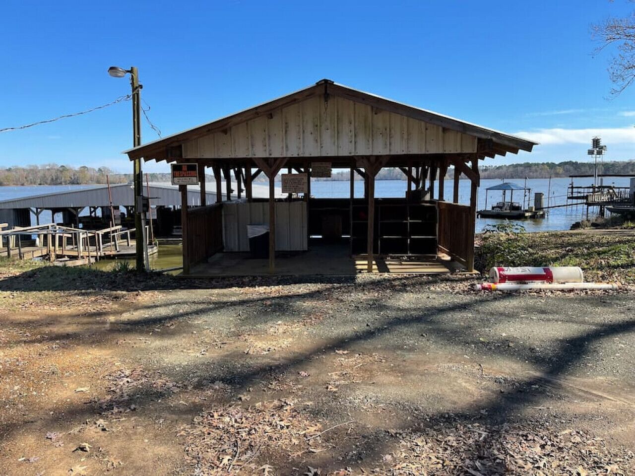 Un pavillon en bois, doté d’un toit, situé sur un terrain recouvert de gravier, près d’une étendue d’eau.