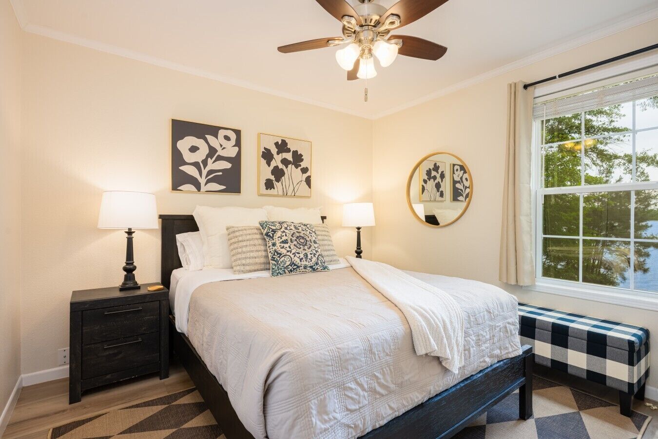 A bedroom with a bed, two bedside tables, a ceiling fan, a window with curtains, and wall art.