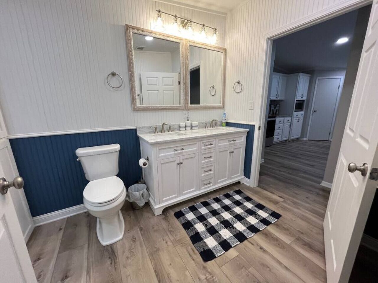 A bathroom with a white toilet, a white vanity with drawers, a mirror above the vanity, and a black and white checkered rug on the floor.