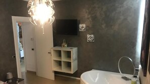 A modern bedroom with a large bed, a built-in TV, a vanity with a mirror, and a bathtub. - Elena's house, is a dream retreat for every type of guest (Sannicandro di Bari)