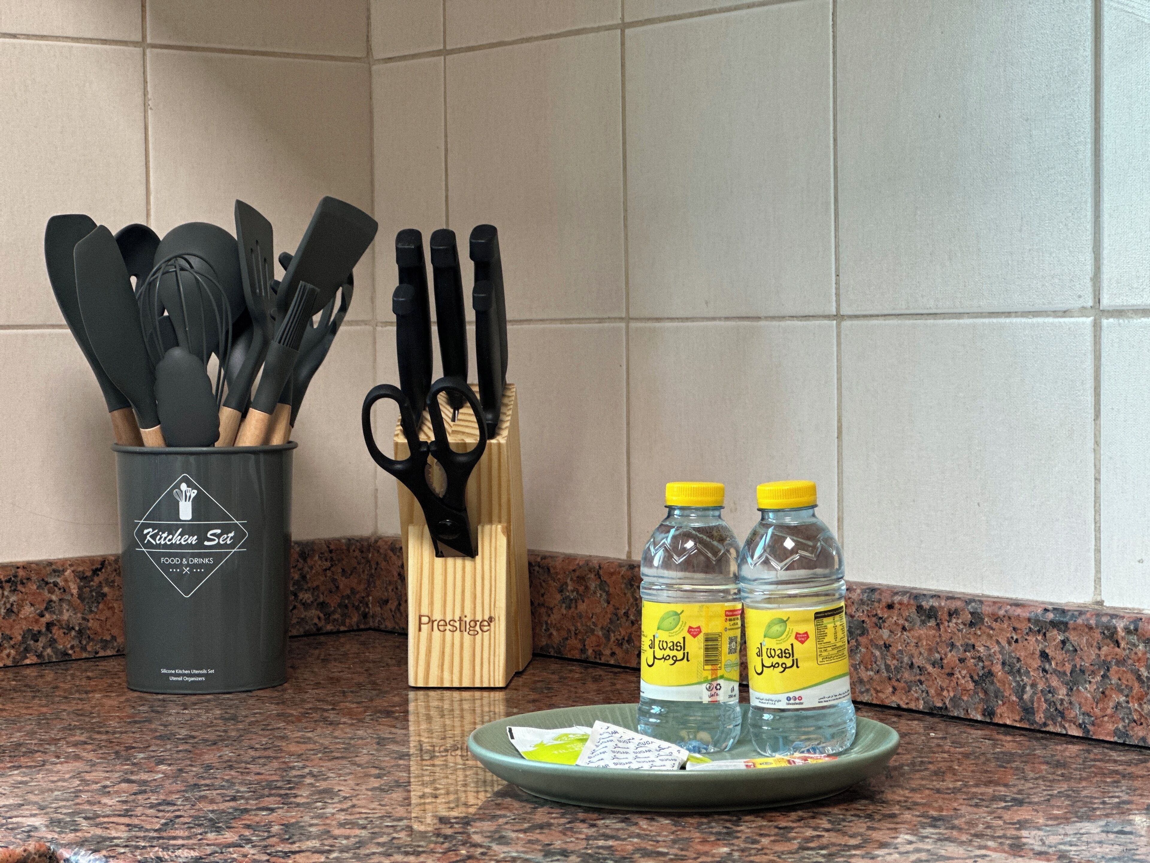 A kitchen counter with a utensil holder, a knife block, and two water bottles.
