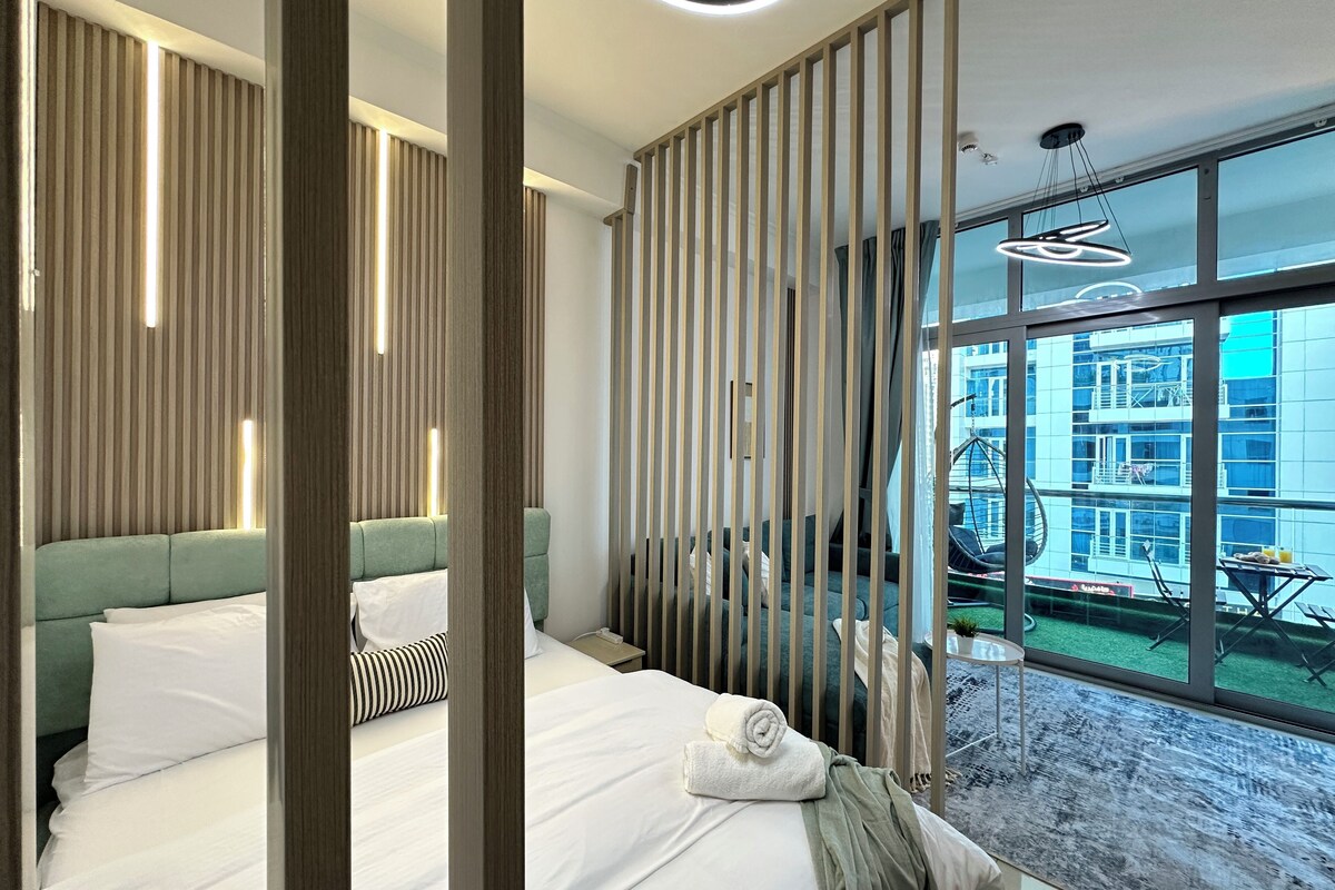A modern hotel room with a large bed, a view of the city, and a balcony with outdoor furniture.