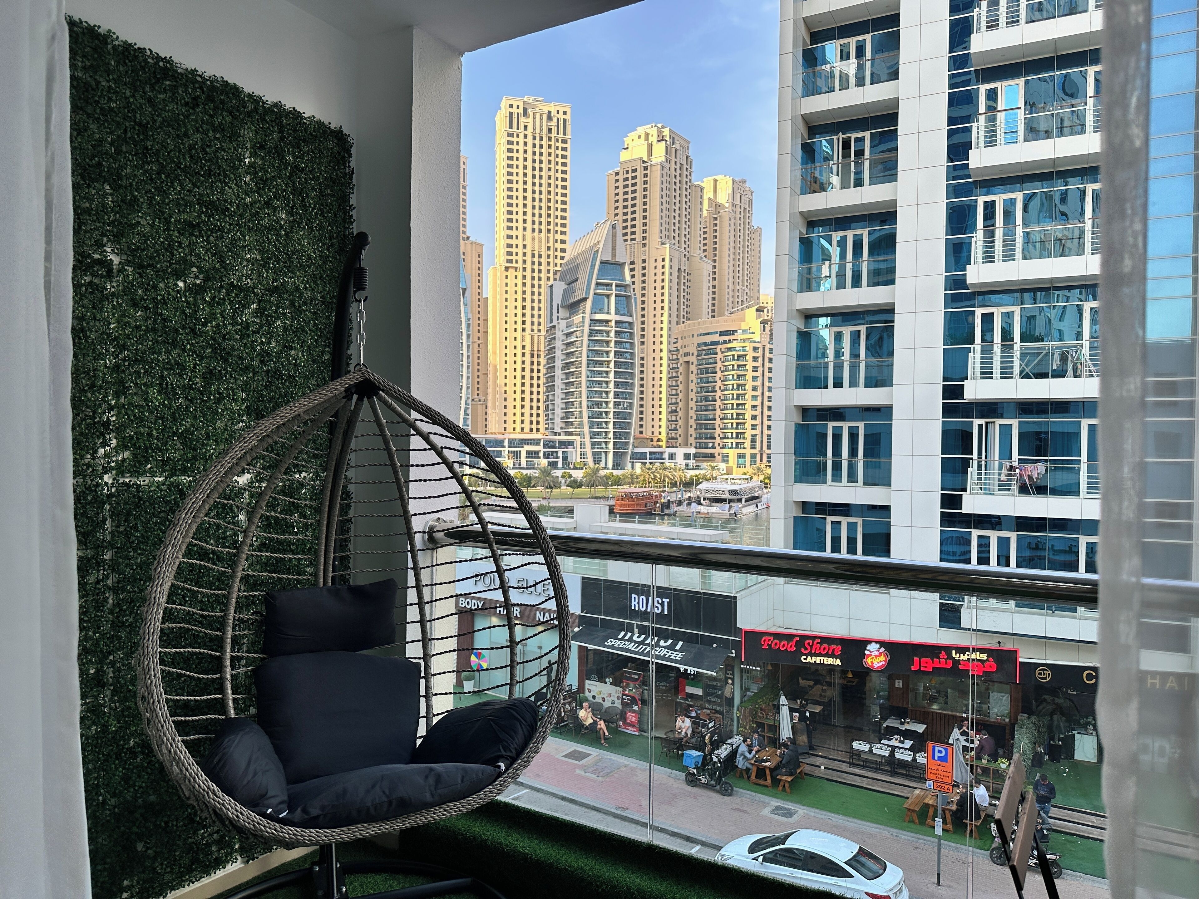 Un intérieur moderne avec un fauteuil suspendu, une vue sur de hauts immeubles et une épicerie de l’autre côté de la rue.