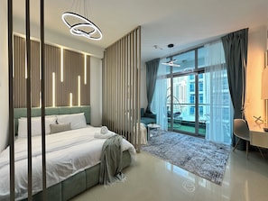 A modern bedroom with a large bed, a desk, and a view of a cityscape through large windows. - Stylish Studio with Stunning Canal View (Dubai)